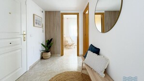 A hallway with a white door, a round mirror, a striped wall, a woven rug, and a bench with a cushion.