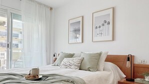 A neatly made bed with a green throw blanket, a bedside table with a lamp, and two framed pictures on the wall.