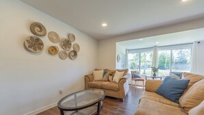 A spacious living room with a beige sofa, a glass coffee table, and a wall adorned with woven wall art. - Timber Lodge Walkable to shops, shoreline & craft beer (Douglas)