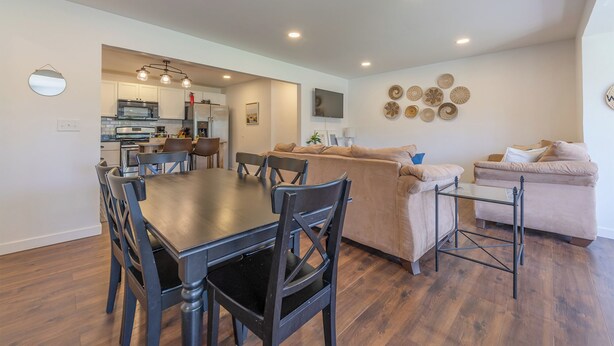 A modern kitchen with white cabinets, a dining table with chairs, a sofa, and a TV mounted on the wall. - Timber Lodge Walkable to shops, shoreline & craft beer (Douglas)