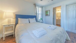 A neatly made bed with a white duvet and a folded towel, a bedside table with a lamp, and a ceiling fan. - Discover comfort at Pine Cove, a cozy 1-bedroom retreat in scenic Douglas, MI. (Douglas)