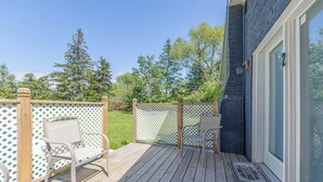 A wooden deck with two chairs, a white lattice fence, and a dark building facade. - Hickory Cottage: Cozy 2-Bedroom in Douglas, MI, close to beaches, downtown, antiques and more!* (Douglas)