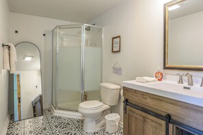 A bathroom with a glass-enclosed shower, a toilet, a sink with a mirror, and patterned floor tiles.