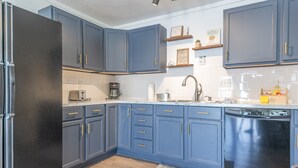 A modern kitchen with blue cabinets, a refrigerator, a dishwasher, and a coffee maker. - Hickory Cottage: Cozy 2-Bedroom in Douglas, MI, close to beaches, downtown, antiques and more!* (Douglas)