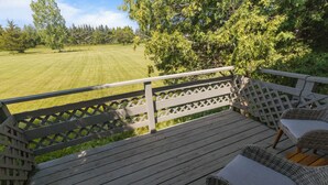 Una terraza de madera con mobiliario de mimbre y vistas a un césped cuidado.