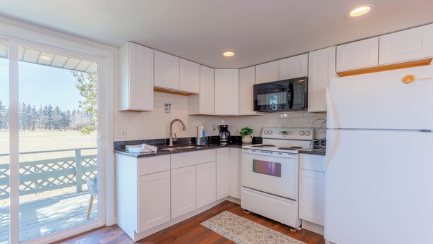 A modern kitchen with white cabinets, a stainless steel microwave, a built-in oven, and a refrigerator. - Maple Getaway -Upstairs Apt. Walk to Downtown, Beaches & Breweries (Douglas)