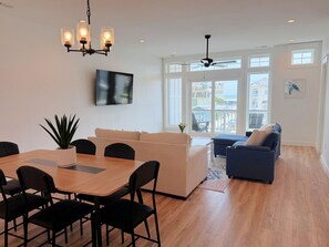 A spacious living area with a dining table, sofas, and a ceiling fan.