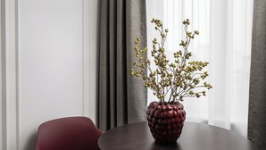 Una mesa redonda con acabado de madera oscura, una silla roja y un jarrón decorativo con ramas y bayas.