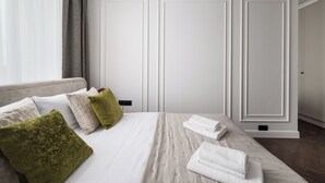 Una cama bien tendida con sábanas blancas y una almohada verde, una mesita de noche con una lámpara y un armario blanco en una habitación de hotel.