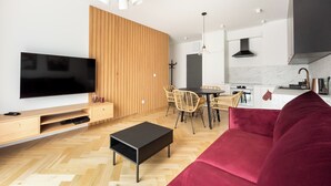 Una sala de estar moderna con televisor de pantalla plana, pared revestida de madera, zona de comedor con sillas y un sofá rojo.