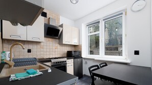 A compact kitchen with a gas stove, microwave, and a small refrigerator. There is a window providing natural light and a view of the outside.