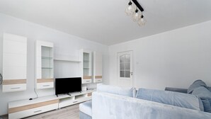 A modern living room with a flat-screen TV, built-in shelving, a light blue sofa, and a white door.