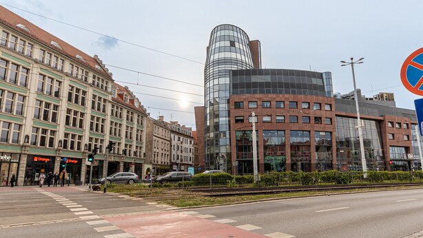 A street with a mix of historic and modern buildings, including a prominent curved glass building.