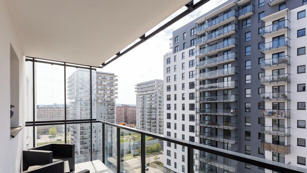 A balcony with a view of high-rise buildings, a glass railing, and outdoor furniture.