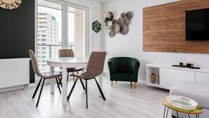 A modern living room with a dining area, a green armchair, a wooden wall panel, and a large clock.