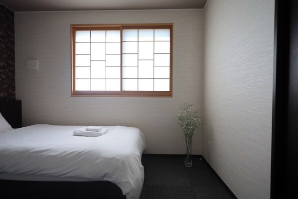 Ein kleiner, sauberer Raum mit einem Bett, einem Fenster und einer Vase mit Blumen.