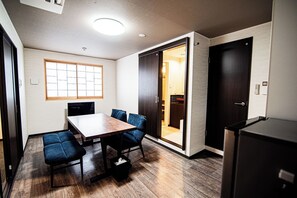 Ein modernes Zimmer mit einem Holztisch, blauen Sitzmöbeln, einem schwarzen Kühlschrank und einer Schiebetür zu einem Küchenbereich.