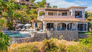 Ein mehrstöckiges Haus mit Pool, Sitzgelegenheiten im Freien und einer Steinmauer.