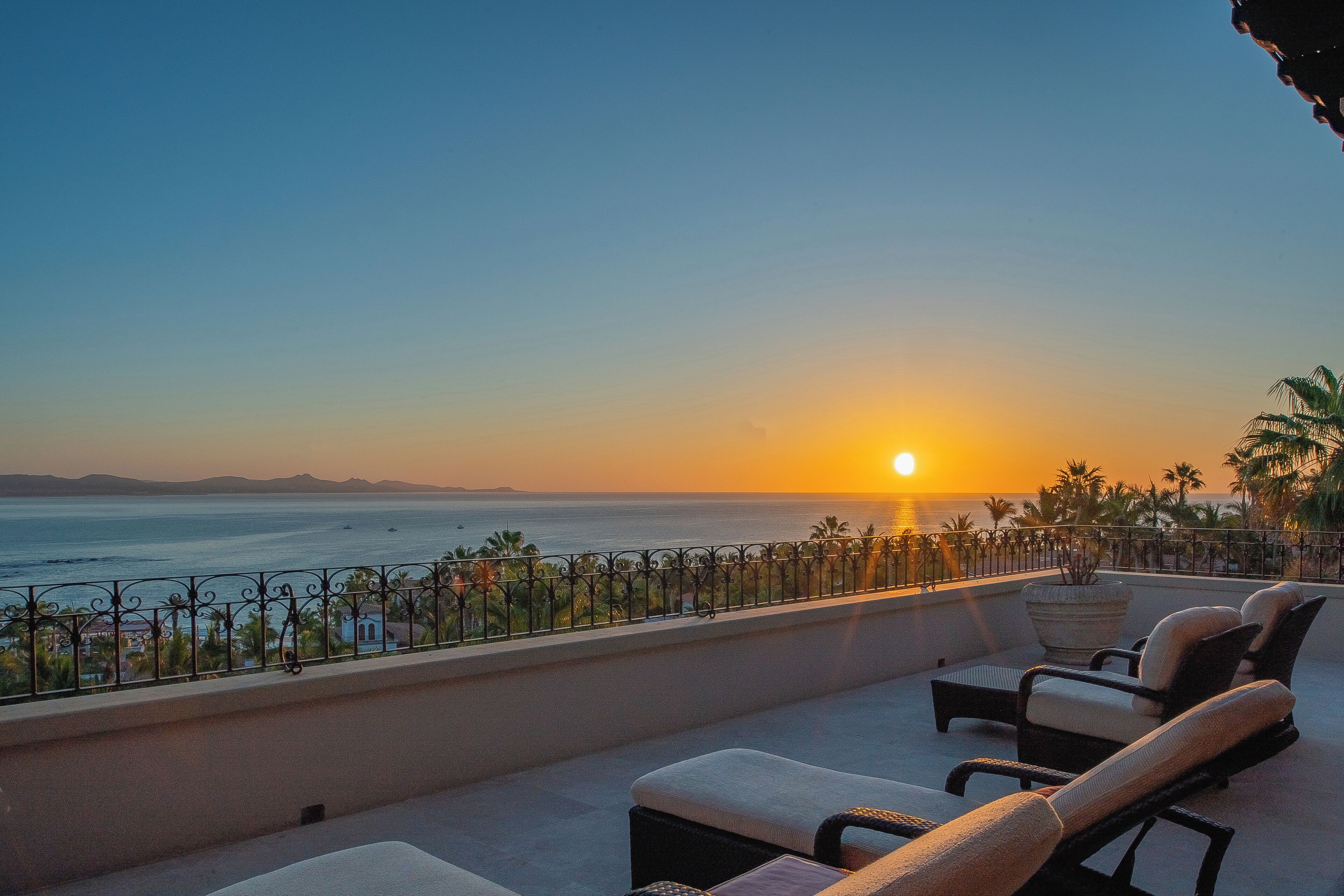Ein Balkon mit Liegestühlen mit Blick auf einen Sonnenuntergang über dem Meer.