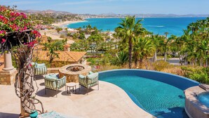 Ein Poolbereich mit geschwungener Kante, Sitzgelegenheiten im Freien und Blick auf Strand und Meer.