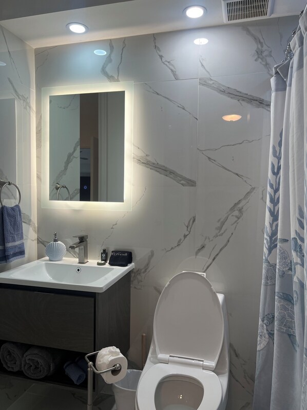 Un bagno con una parete in marmo, un lavandino, un water e una tenda da doccia.