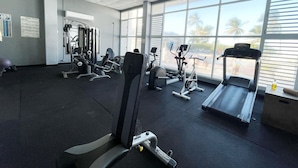 A gym with various exercise equipment, large windows, and a view of palm trees.