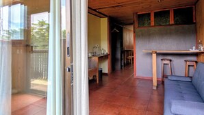 A modern interior with a wooden ceiling, a sliding glass door leading to a balcony, a kitchen area with a bar, and a seating area with a sofa. - Miztli Lodge & Adventures (Monteverde)