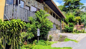 A two-story building with a stone facade, multiple windows, and a balcony with a wooden railing. - Miztli Lodge & Adventures (Monteverde)