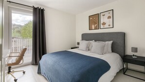 Un dormitorio moderno con una cama grande, una silla junto a la ventana y dos obras de arte en la pared.
