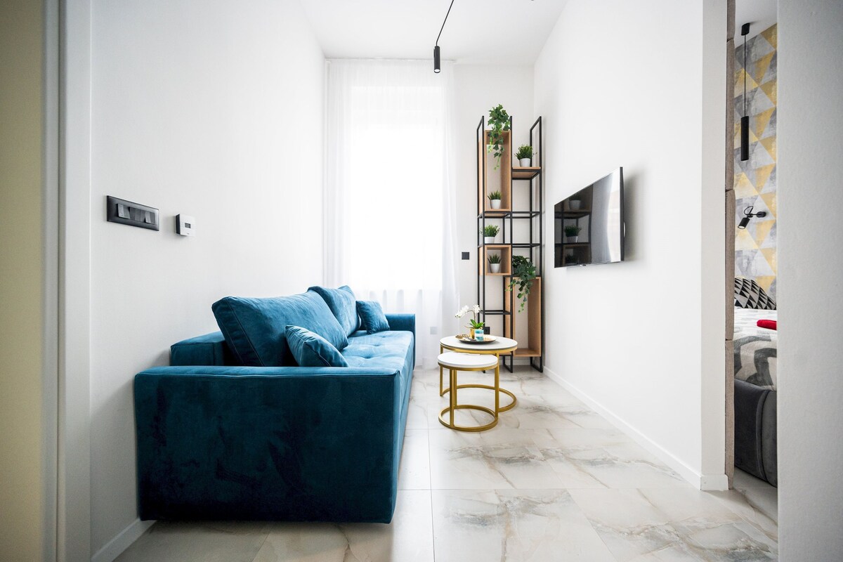 A modern living room with a blue sofa, a small round table, and a TV mounted on the wall.