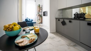 Una cucina moderna con zona pranzo, che include un tavolo imbandito con cibo e bevande, un divano blu e una scala che conduce a un'altra stanza.