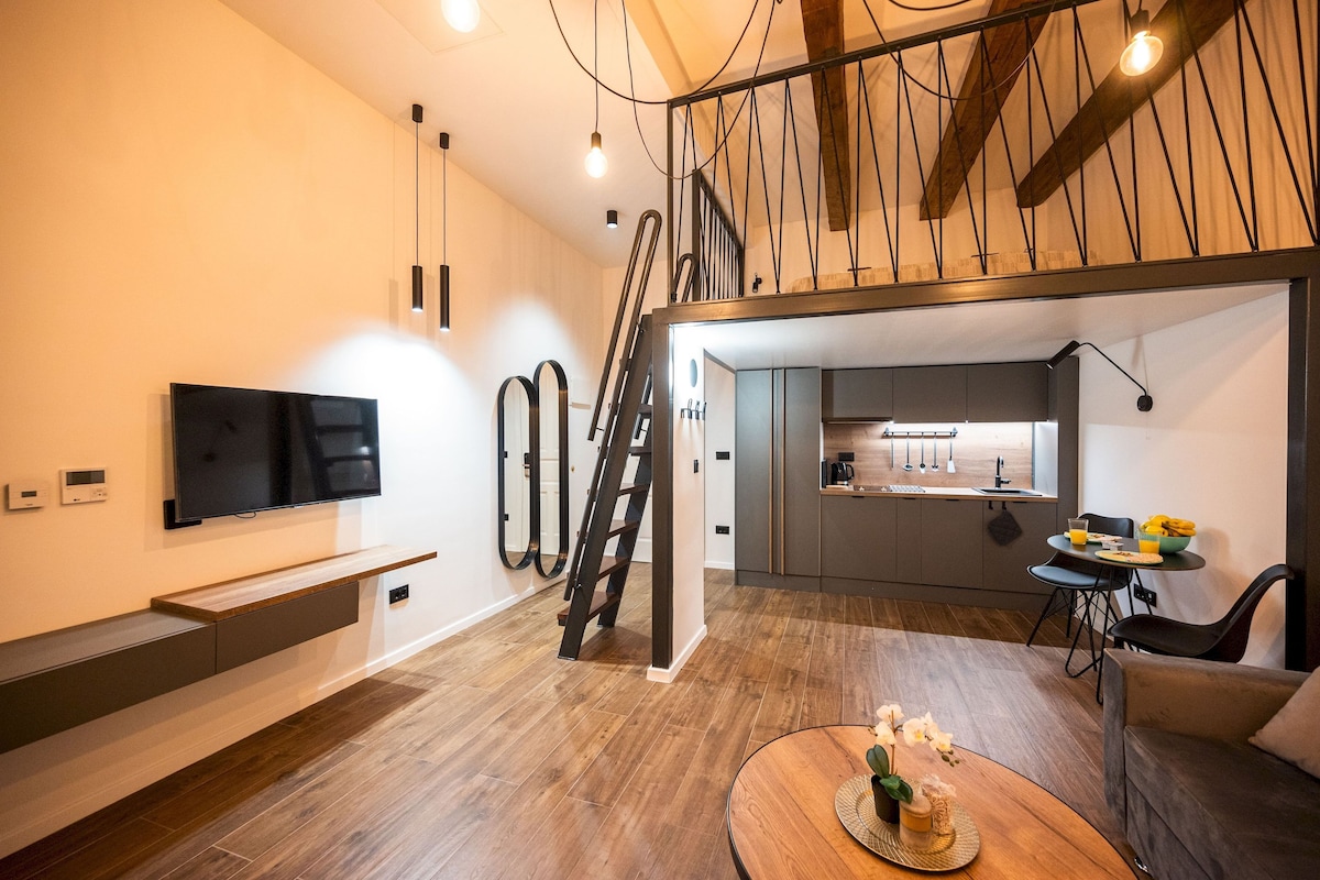 A modern living room with a flat-screen TV, a staircase, a kitchen area, and a dining space with a table and chairs.