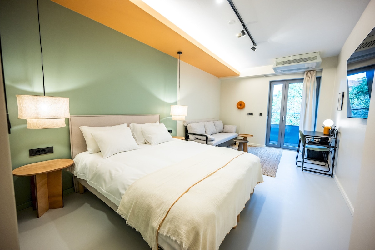 A modern bedroom with a large bed, bedside lamps, a small table, and a sofa.