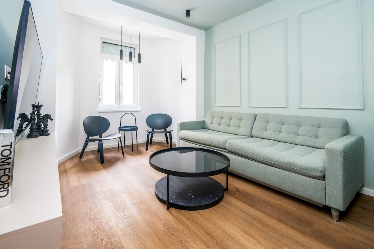 A modern living room with a sofa, two chairs, a round coffee table, and a window.