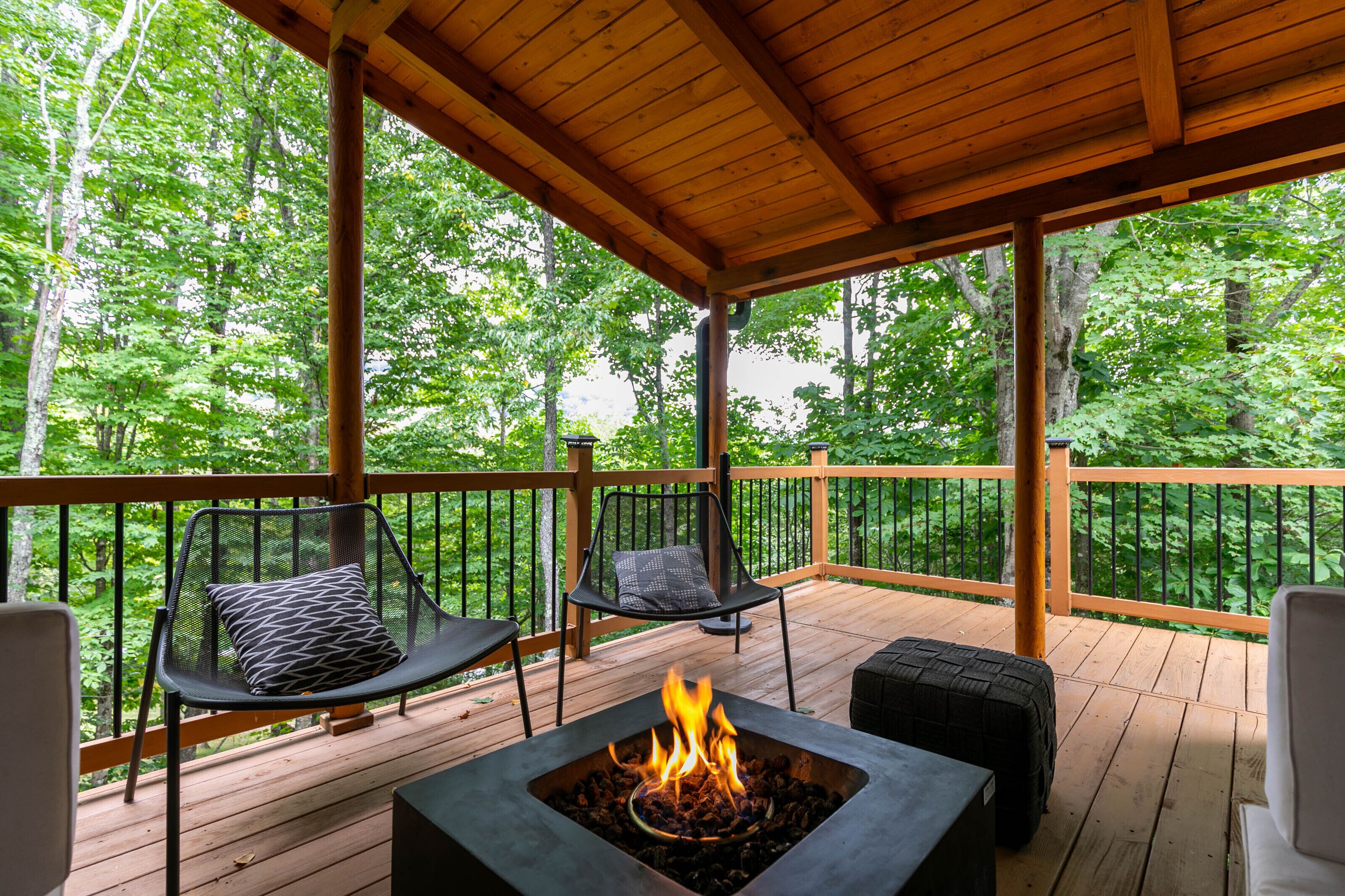 Une terrasse couverte avec un foyer, deux chaises et une vue sur une forêt.