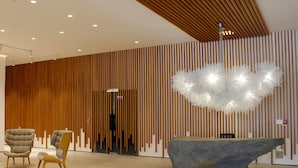 Un interior moderno con listones verticales de madera, una gran lámpara escultórica y dos sillones tapizados.