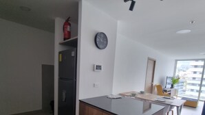 Una cocina moderna con una isla central, horno integrado y refrigerador. Hay un reloj en la pared y una ventana que proporciona luz natural.