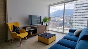 Una sala moderna con un ventanal grande, un sofá, un televisor y un sillón amarillo.