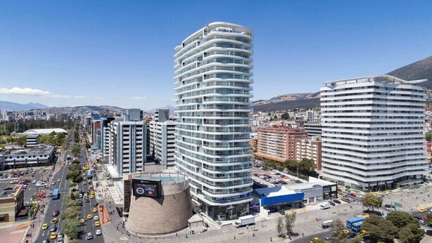 Un edificio moderno de varios pisos con fachada curva, rodeado de otros edificios altos y una calle urbana concurrida.