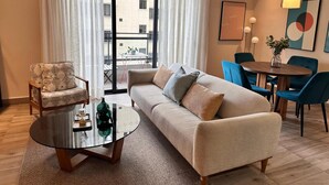 Un salon moderne avec un canapé, un fauteuil et une table basse ronde. Il y a un balcon avec une table et des chaises à l'extérieur.