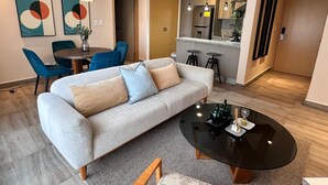 Un salon moderne avec un canapé gris, une table basse ronde et un coin repas avec des chaises bleues.