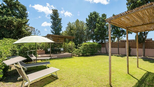 Um quintal com pérgola, mesa e cadeiras, e uma poltrona.