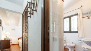 Casa de banho com azulejos brancos, sanita, bidé e lavatório.