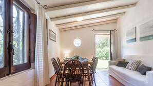 A dining area with a wooden table and chairs, a lamp, and a view of the garden through the open door.