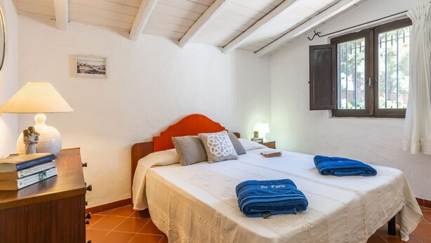 A bedroom with a bed, a nightstand, a lamp, and a window with curtains.