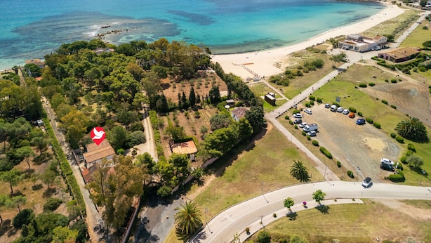 An aerial view of a coastal area with a beach, a small island with a structure, and a road with parked cars. - Villa Angela by Interhome (Pula)