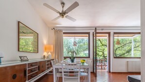 A dining area with a table and chairs, a ceiling fan, a window with curtains, and a view of trees outside. - Villa Angela by Interhome (Pula)