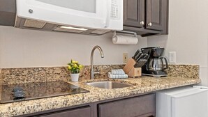 Una cocina con encimeras de granito, un lavamanos de acero inoxidable, microondas integrado, cafetera y bloque de cuchillos.