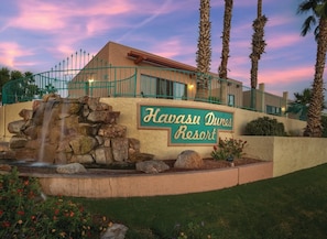 A resort building with a sign reading 'Havasu Dunes Resort,' a waterfall feature, and palm trees.
