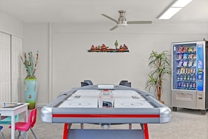 Ein Zimmer mit Billardtisch, Deckenventilator, einer an der Wand befestigten Ablage mit Dekorationsobjekten, einer Verkaufsmaschine und einer Topfpflanze.